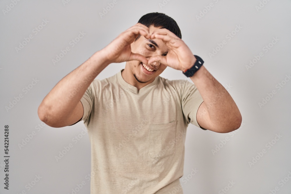 Young arab man wearing casual t shirt doing heart shape with hand and fingers smiling looking through sign Young arab man wearing casual t shirt doing heart shape with hand and fingers smiling looking through sign