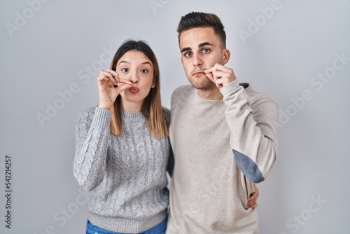 Young hispanic couple standing over white background mouth and lips shut as zip with fingers. secret and silent, taboo talking