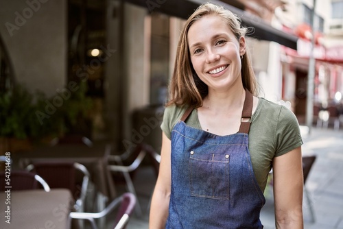 Young blonde woman smiling happy wearing apron at coffee shop