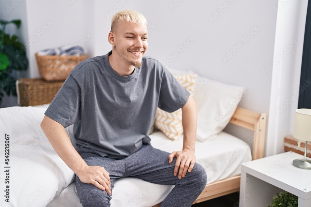 Young caucasian man smiling confident sitting on bed at bedroom