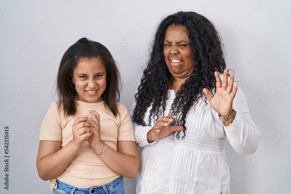 Mother and young daughter standing over white background disgusted expression, displeased and fearful doing disgust face because aversion reaction. Mother and young daughter standing over white background disgusted expression, displeased and fearful doing disgust face because aversion reaction.