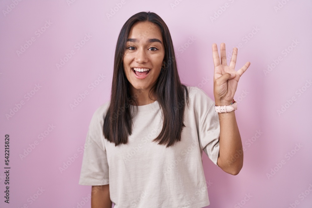 Young hispanic woman standing over pink background showing and pointing up with fingers number four while smiling confident and happy. Young hispanic woman standing over pink background showing and pointing up with fingers number four while smiling confident and happy.