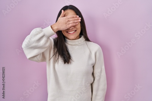 Young south asian woman standing over pink background smiling and laughing with hand on face covering eyes for surprise. blind concept. © Krakenimages.com