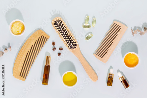 Hair care flat lay with wooden combs, ingredients for mask for hair, vitamins for health hair and natural oils on a blue background. Natural beauty products for health hair