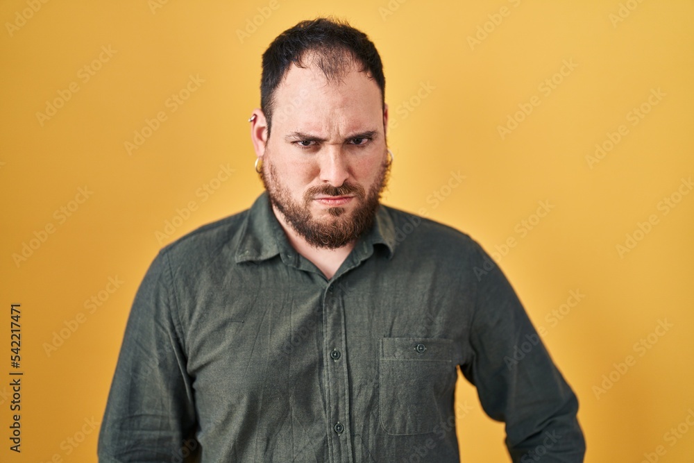 Plus size hispanic man with beard standing over yellow background skeptic and nervous, frowning upset because of problem. negative person. Plus size hispanic man with beard standing over yellow background skeptic and nervous, frowning upset because of problem. negative person.