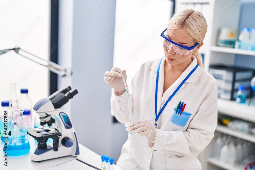 Young blonde woman wearing scientist uniform measuring liquid at laboratory Young blonde woman wearing scientist uniform measuring liquid at laboratory