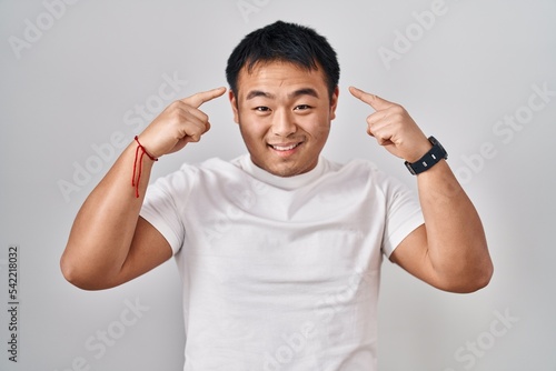 Young chinese man standing over white background smiling pointing to head with both hands finger, great idea or thought, good memory