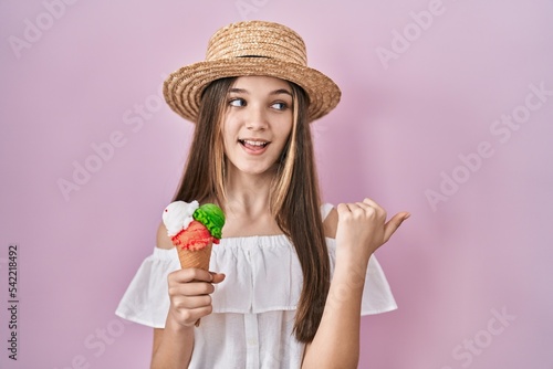 Teenager girl holding ice cream smiling with happy face looking and pointing to the side with thumb up.