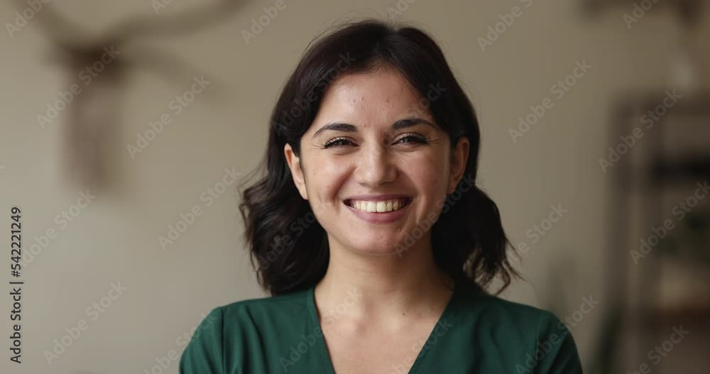 Head shot attractive young brunette woman in casual clothes and wide toothy smile standing indoors, posing staring at camera feels happy. Teacher, professional occupation person or housewife portrait