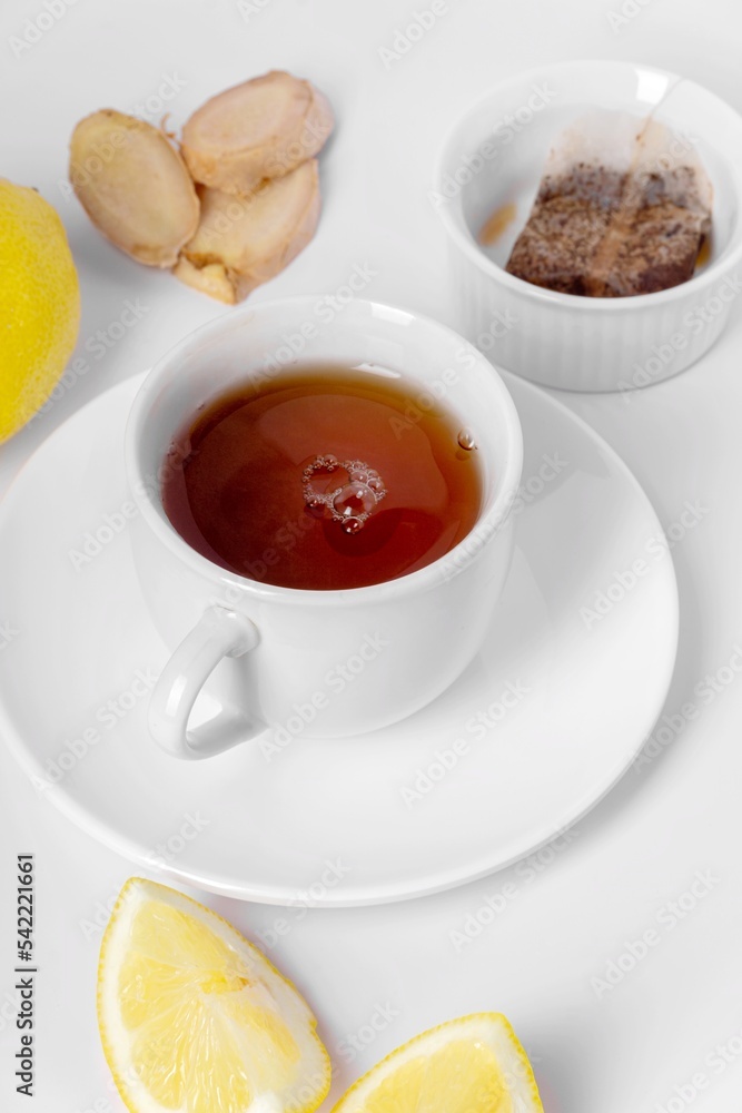 A cup of fresh tea with lemon, ginger, and tea bag. White background, isolated white. Close up. A cup of fresh tea with lemon, ginger, and tea bag. White background, isolated white. Close up.