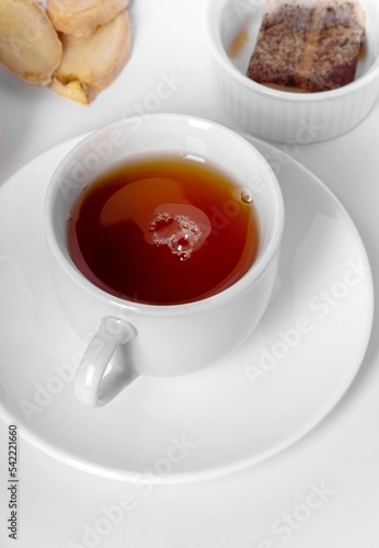 A cup of fresh tea with lemon, ginger, and tea bag. White background, isolated white. Close up.