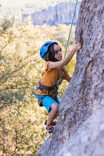Children's rock climbing. The boy climbs a rock against the backdrop of mountains. Extreme hobby. An athletic child trains to be strong.