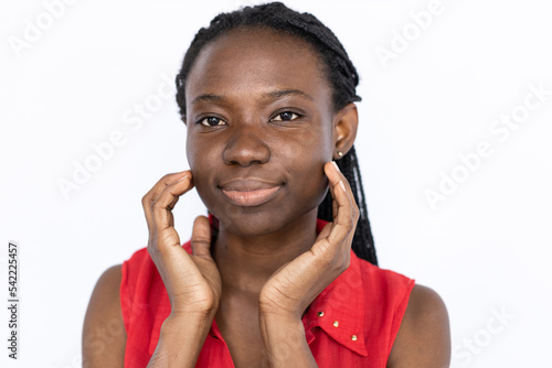 Content woman touching face. Female African American model in red vest looking at camera touching skin on cheeks. Portrait, studio shot, skincare concept