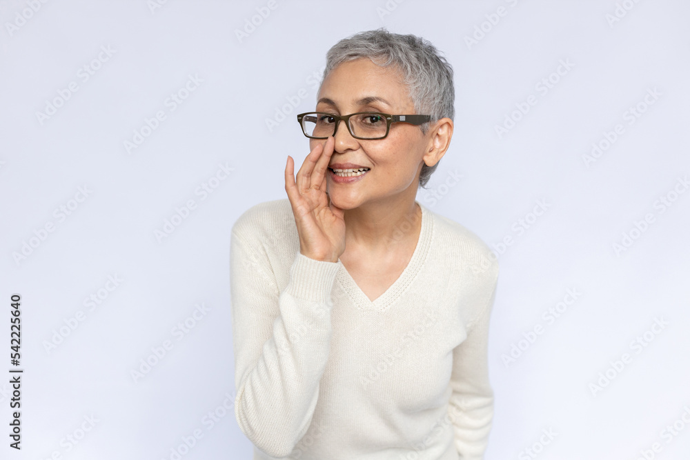 Portrait of conspiring senior woman whispering secret. Mature Caucasian woman wearing eyeglasses and white jumper telling gossip covering mouth with hand. Gossip and secret concept Portrait of conspiring senior woman whispering secret. Mature Caucasian woman wearing eyeglasses and white jumper telling gossip covering mouth with hand. Gossip and secret concept