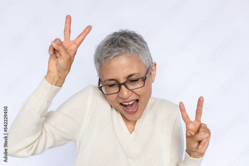 Portrait of joyful senior woman making rock gesture over white background. Mature Caucasian woman wearing eyeglasses and white jumper having fun. Happiness and fun concept Portrait of joyful senior woman making rock gesture over white background. Mature Caucasian woman wearing eyeglasses and white jumper having fun. Happiness and fun concept