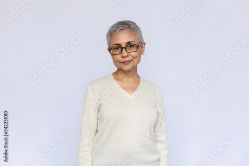 Portrait of serious senior woman wearing eyeglasses and white jumper. Mature Caucasian woman standing and looking at camera over white background. Elderly woman concept