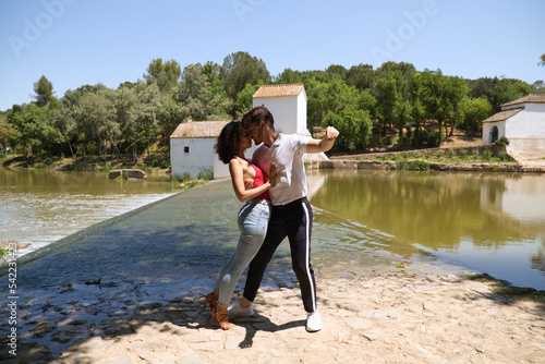 latin loving couple dancing social dance, kizomba, taraxia bachata, semba in the park next to the river and some big trees. Dance concept photo