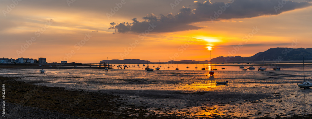 sunrise on the Menai Strait and mountains of Snowdonia at low tide with Beaumaris village in silhouette