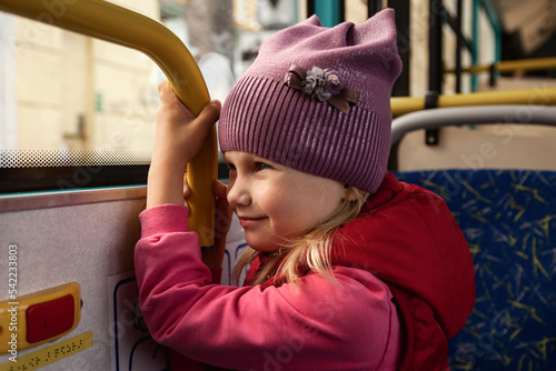 Cute child rides bus of public modern transport looks out window. Little girl in metropolitan transport, sitting on seat, deep thinking. Concept of public transport and urban lifestyle. Copy space