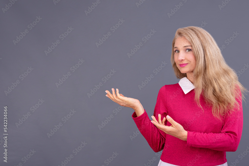 Retrato en plano medio de mujer joven de cabello rubio en actitud positiva señalando con sus manos espacio vacío y fondo gris para publicidad. Retrato en plano medio de mujer joven de cabello rubio en actitud positiva señalando con sus manos espacio vacío y fondo gris para publicidad.