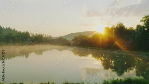 Lake filmed in the morning with the drone of the sunrise of the yellow sun and the clear sky in a green forest. photo