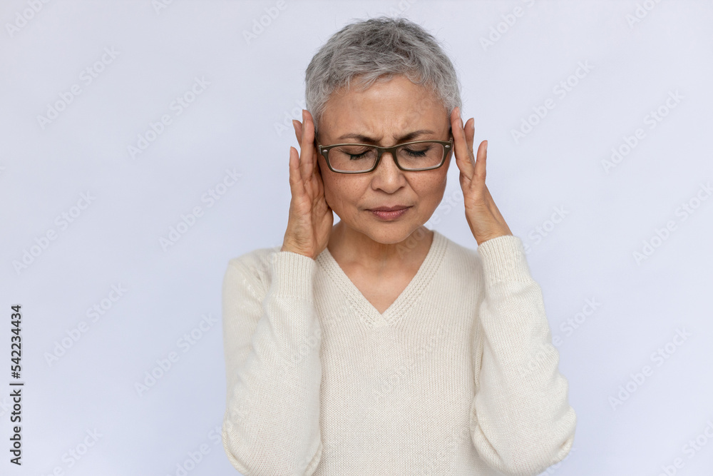 Portrait of sad senior woman suffering from headache. Mature Caucasian woman wearing eyeglasses and white jumper frowning of pain and touching head. Migraine concept Portrait of sad senior woman suffering from headache. Mature Caucasian woman wearing eyeglasses and white jumper frowning of pain and touching head. Migraine concept