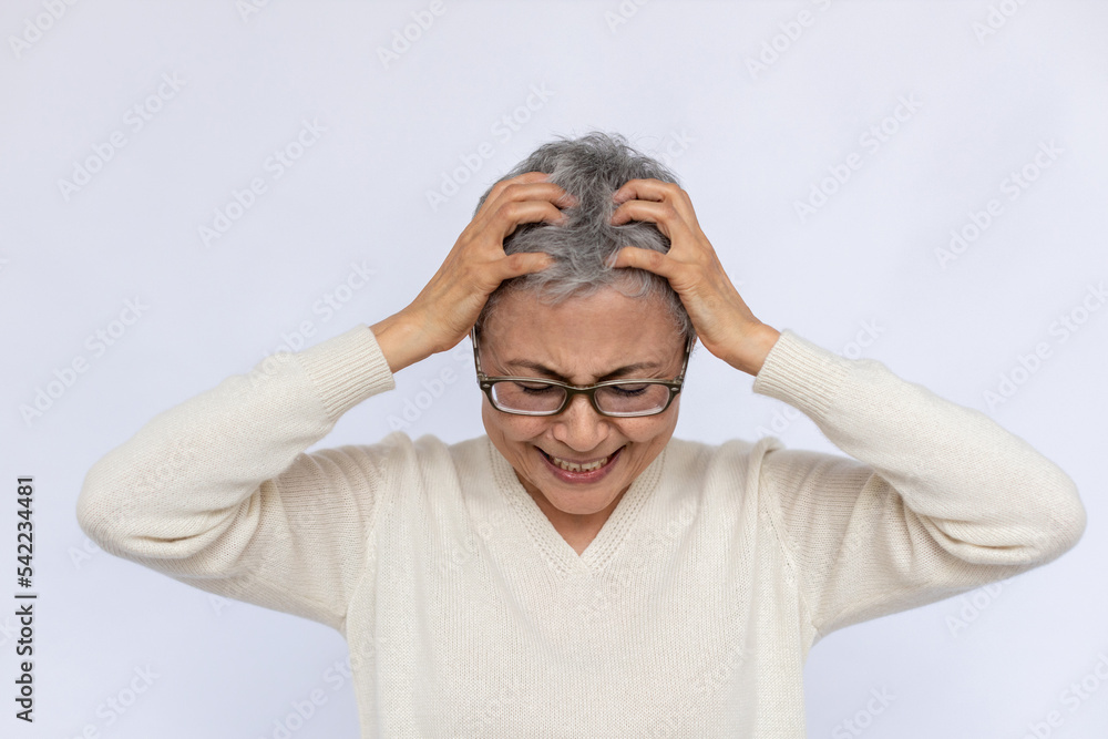 Portrait of frustrated senior woman holding head in hands. Mature Caucasian woman wearing eyeglasses and white jumper crying over white background. Despair, grief, trouble concept Portrait of frustrated senior woman holding head in hands. Mature Caucasian woman wearing eyeglasses and white jumper crying over white background. Despair, grief, trouble concept