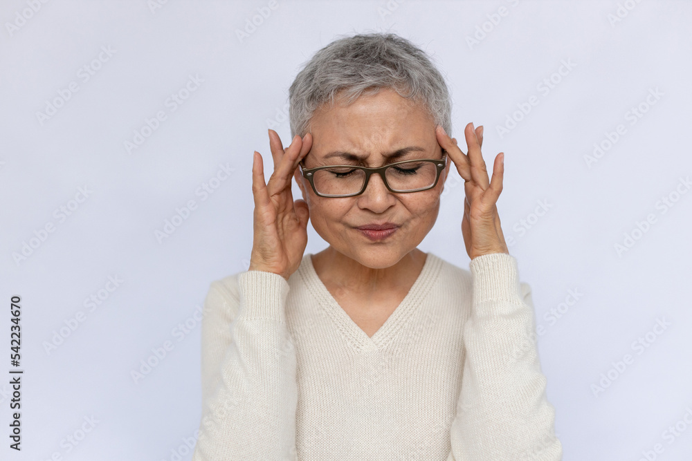 Portrait of unwell senior woman suffering from migraine. Mature Caucasian woman wearing eyeglasses and white jumper touching aching temples. Headache concept Portrait of unwell senior woman suffering from migraine. Mature Caucasian woman wearing eyeglasses and white jumper touching aching temples. Headache concept