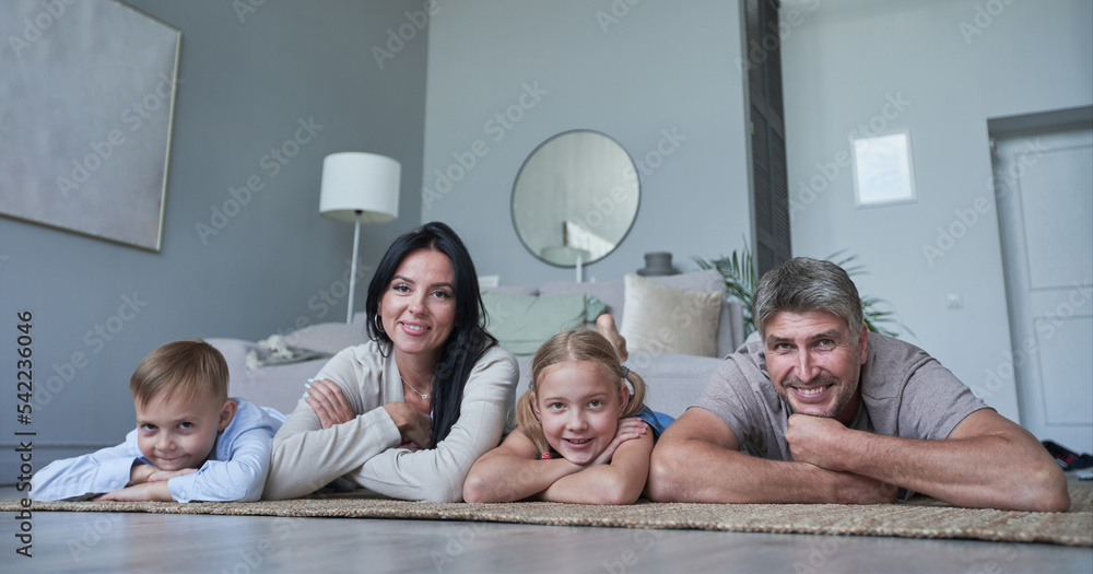 Photo of four members adopted family lying floor toothy smiling fluffy carpet cozy apartments - obrazy, fototapety, plakaty 