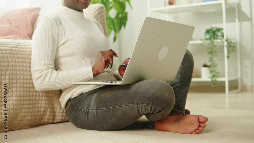 Native African American woman using laptop close-up. Young female student working remotely at computer in living room, freelancer. Remote work. Communicating with friends via internet. Native African American woman using laptop close-up. Young female student working remotely at computer in living room, freelancer. Remote work. Communicating with friends via internet.