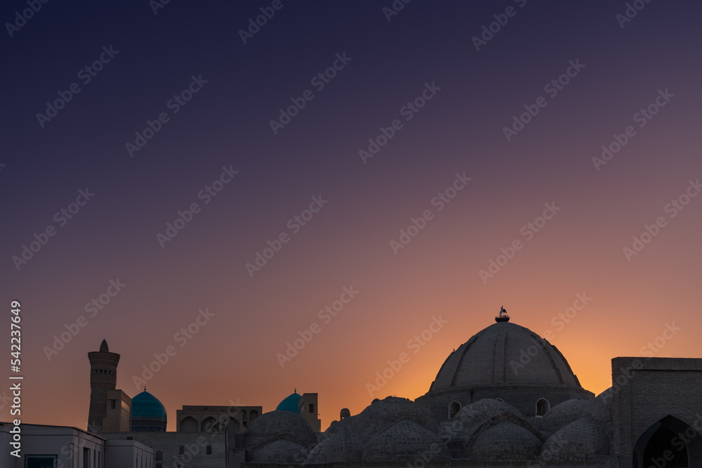 Old Uzbek city skyline with silhouette of big dome and minaret against sunset sky Bukhara Uzbekistan