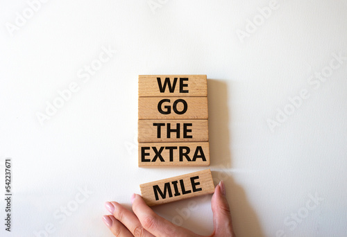 We go the extra mile symbol. Wooden blocks with words We go the extra mile. Beautiful white background. Businessman hand. Business and We go the extra mile concept. Copy space.