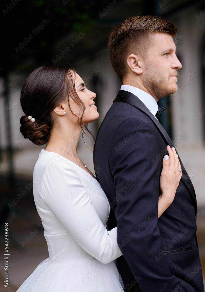 Pretty young bride woman in white elegant dress hugging groom from the back. Wedding day ceremony outdoors, happy loving brides. Сreating a family. Marriage. Married couple. Pretty young bride woman in white elegant dress hugging groom from the back. Wedding day ceremony outdoors, happy loving brides. Сreating a family. Marriage. Married couple.