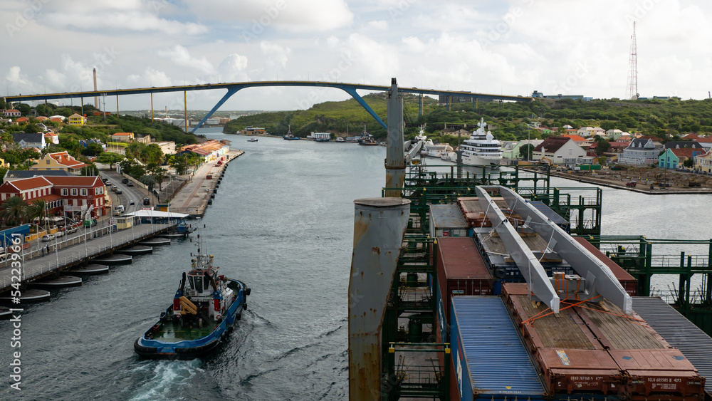 Willemstad, Curacao - 04.28.2021 Container ship passing under Queen Juliana bridge  with tug assistance in Willemstad, Curacao