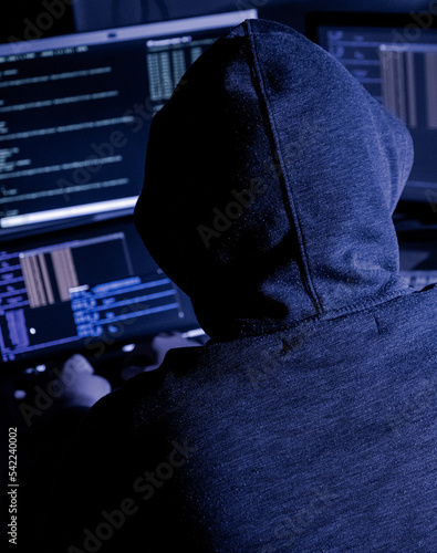 Hooded hacker attempting data breach at night in a dark private office