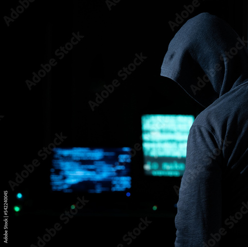 Hooded hacker looming in the dark of a computer room