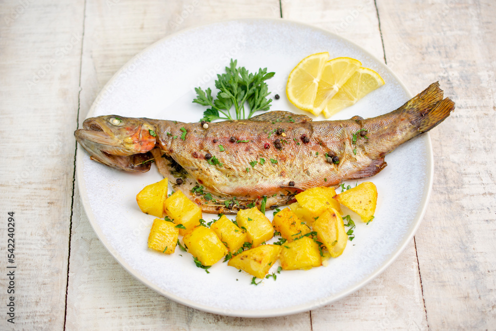 Baked trout with potato in plate. Wooden table.