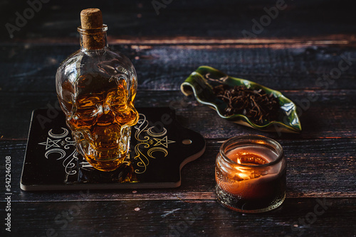 Close up shot of a skull shaped transparent bottle filled with strong alcohol. Alcoholic beverage on wooden background. Dark mystique atmosphere with candle light. Dimming light. Low Key Photography.  photo