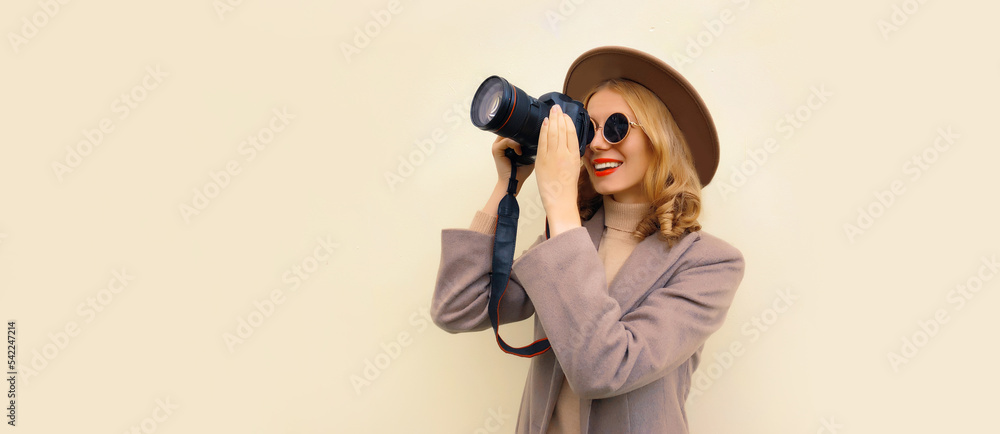 Portrait of stylish happy smiling woman photographer with digital camera taking picture wearing round hat, brown coat on background, blank copy space for advertising text Portrait of stylish happy smiling woman photographer with digital camera taking picture wearing round hat, brown coat on background, blank copy space for advertising text