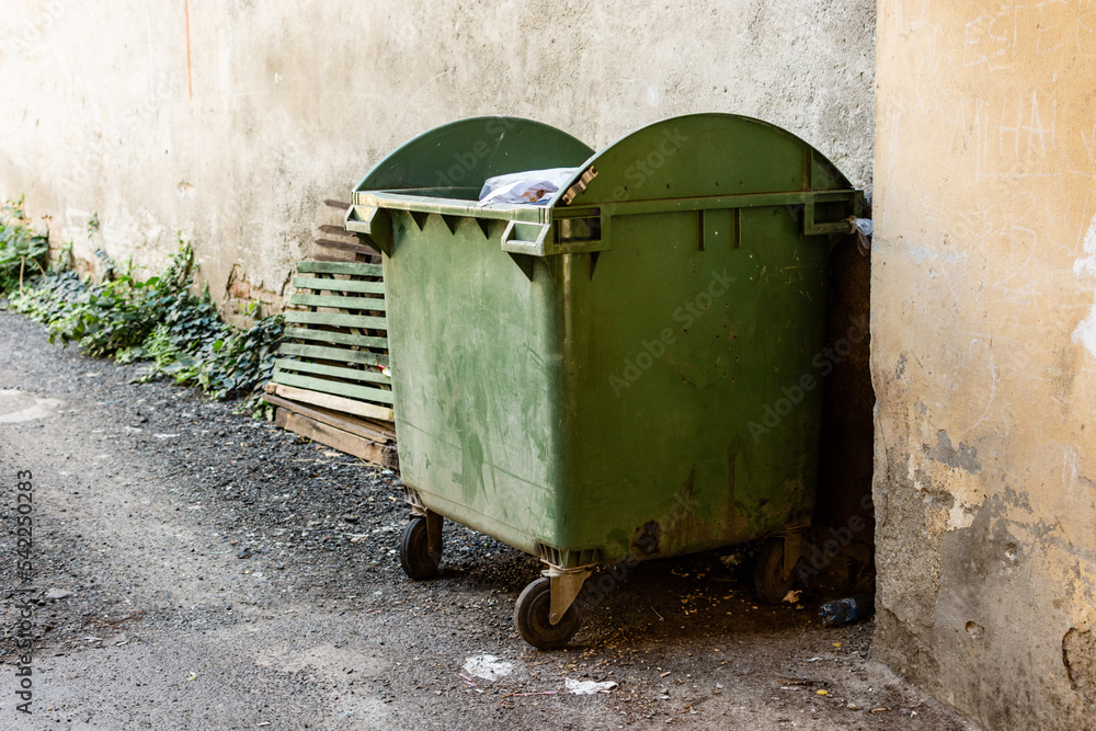 Plastic dirty dumpster next to a grunge wall of an old building in the neighborhood Plastic dirty dumpster next to a grunge wall of an old building in the neighborhood