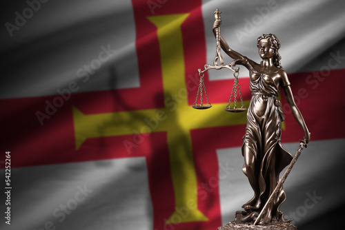 Guernsey flag with statue of lady justice and judicial scales in dark room. Concept of judgement and punishment photo