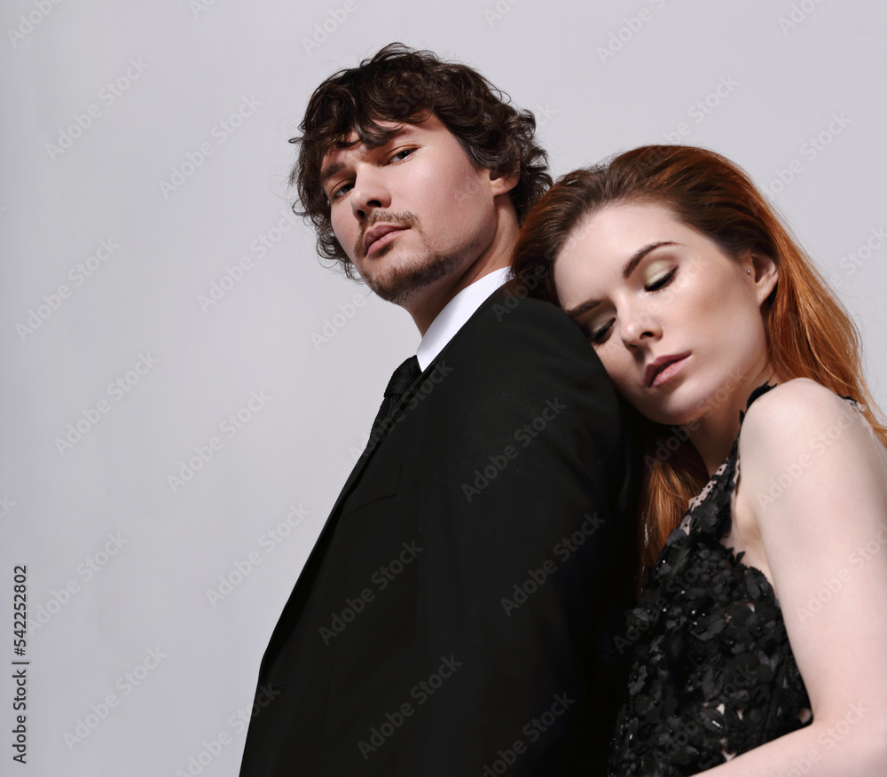 Sexy bright foxy hairstyle female woman in fashion black long skirt dress hugging with sad thinking face her serious handsome man in black suit clothing on light blue studio background. Closeup Sexy bright foxy hairstyle female woman in fashion black long skirt dress hugging with sad thinking face her serious handsome man in black suit clothing on light blue studio background. Closeup