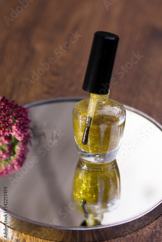 A translucent gold glitter nail polish with a rose red flower that reflects in the mirror.