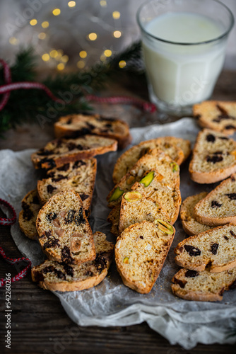 Mix of Italian homemade biskotti with different flavors (chocolate, dried fruits, pistachios ) and glass of milk on wooden table.