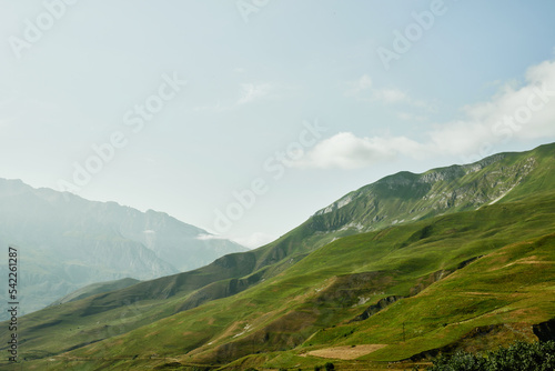 Mountain peaks covered with green meadows and clouds above them. Midday in mountains. North Ossetia-Alania, Russia.