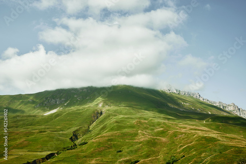 Mountain peaks covered with green meadows and clouds above them. Midday in mountains. North Ossetia-Alania, Russia.