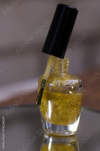 A bottle of translucent gold glitter nail polish on a mirror surface