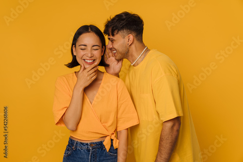 Young stylish smiling man whispering to beautiful laughing asian woman