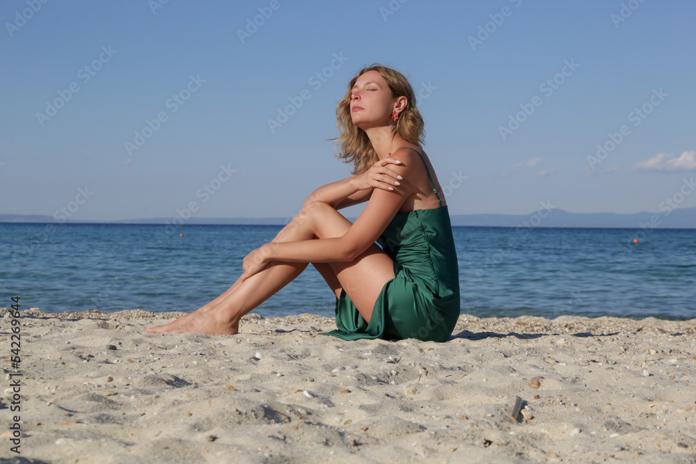 Beautiful young model in camisole emerald green silk satin long dress, fashion summer portrait on the beach	