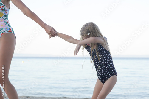 Mother pulling stubborn toddler girl on the beach. Girl does not want to leave. Problem of leaving the beach.